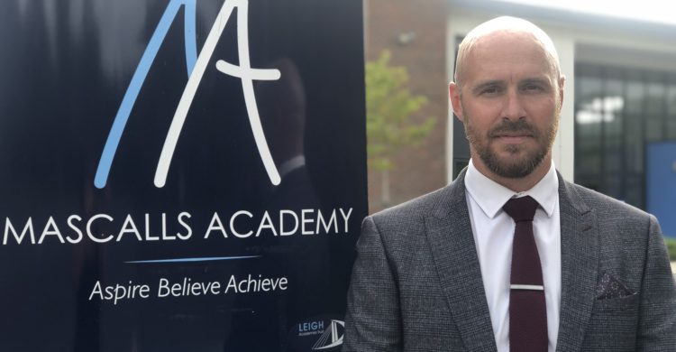Photo of Mascalls Academy Principal, Mr Will Monk standing next to a sign with the academy logo.
