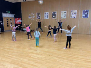 Two students are seen instructing younger children on how to dance in the activity hall at Mascalls Academy.