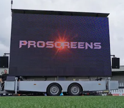 An outdoor cinema system is seen parked on a field with the word 'Proscreens' shown on the screen.