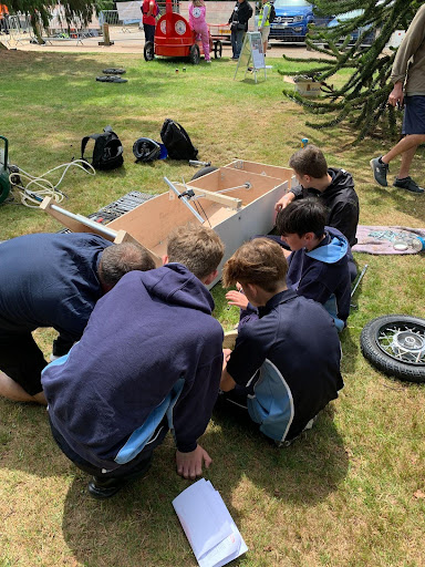 Four students are seen working with a member of staff to build a lifesize wooden car.
