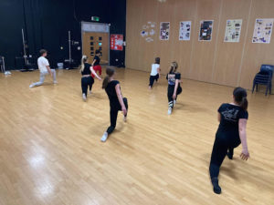 A group of Sixth Form students can be seen participating in a Dance lesson in the auditorium.