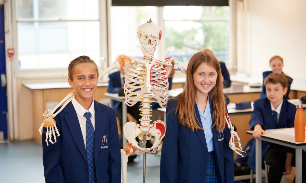 Two students with a skeleton smiling in a classroom