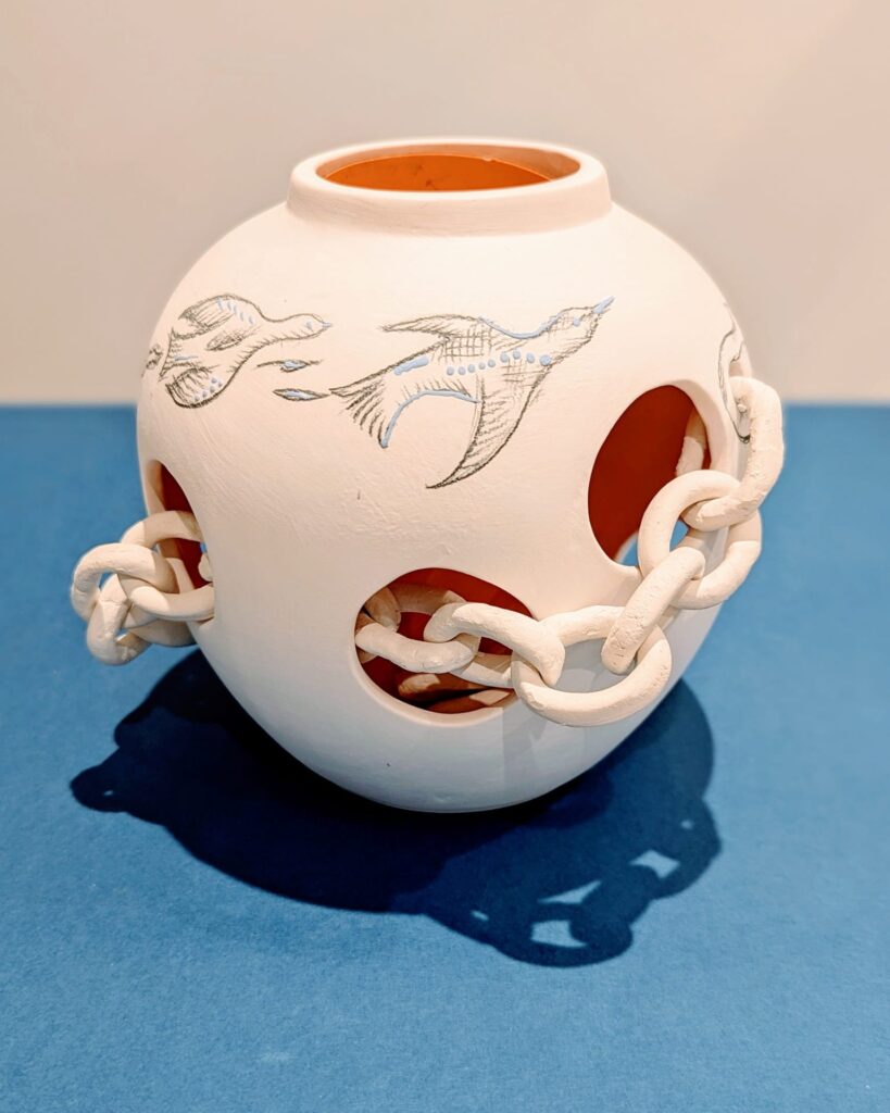 A clay urn with a chain around it and drawings of birds